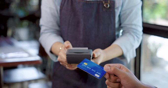 Close up credit card payment between customer and elderly cafe owner in apron holding card reader, teamwork hospitality concept showing small business service and modern payment method in restaurant