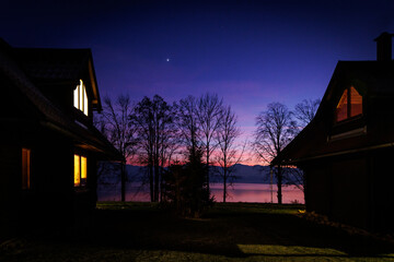 Lakeside houses at dusk with glowing windows and twilight sky