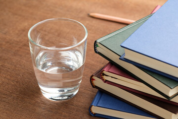 Glass half full of water placed beside a stack of books symbolizing open-minded learning attitude,...