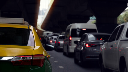 Rear side of taxi car two tone color yellow and green. Traffic jam in the city with cars on the asphalt road. Above is a silhouette of a different level road. Traffic in the bangkok of Thailand.