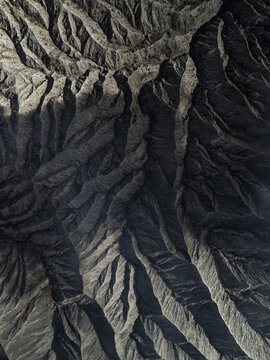Aerial view of stark, dramatic ridges cast in deep shadows, revealing the rugged terrain of Mount Bromo, East Java, Indonesia.