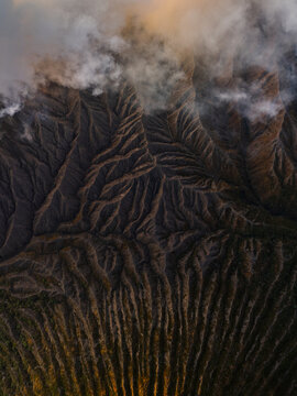 Aerial view of stark, dramatic ridges and valleys carved into the landscape, shrouded in ethereal mist and clouds, Mount Bromo, East Java, Indonesia.