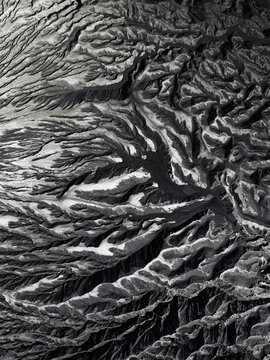 Aerial view of a stark, rugged landscape carved by deep valleys and shadowed peaks, revealing nature's monochrome artistry, Mount Bromo, East Java, Indonesia.
