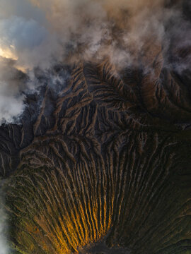 Aerial view of the rugged terrain and wispy clouds meet in a dramatic dance of light and shadow over Mount Bromo, East Java, Indonesia.