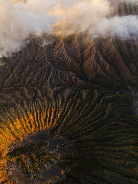 Aerial view of the rugged, sun-kissed terrain contrasts dramatically with the shadowy depths of Mount Bromo, East Java, Indonesia.