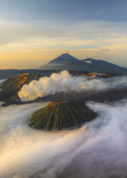 Aerial view of Mount Bromo's volcanic landscape shrouded in mist and bathed in the warm glow of sunrise, East Java, Indonesia.