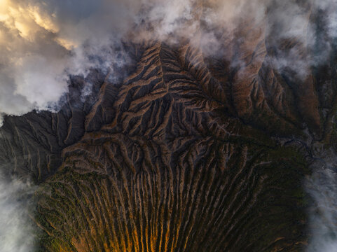 Aerial view of the rugged, textured landscape of Mount Bromo shrouded in ethereal clouds, East Java, Indonesia.
