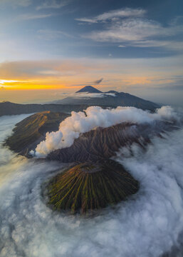 Aerial view of the majestic Mount Bromo and surrounding volcanic landscape piercing through a sea of clouds as dawn paints the sky in vibrant hues, Mount Bromo, East Java, Indonesia.