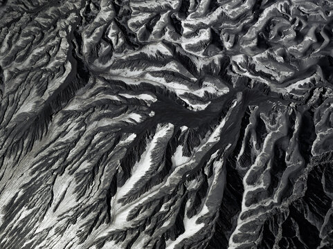 Aerial view of a stark, monochrome landscape, where deep shadows carve intricate patterns amidst the undulating terrain, Mount Bromo, East Java, Indonesia.