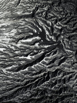 Aerial view of an abstract landscape of volcanic terrain, revealing a tapestry of deep shadows and bright highlights across the rugged surface, Mount Bromo, East Java, Indonesia.