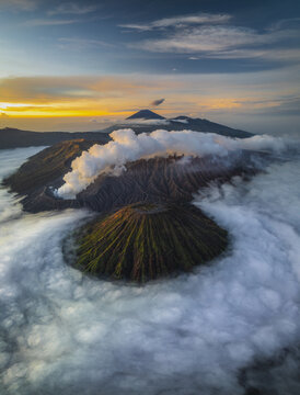 Aerial view of the majestic Mount Bromo piercing through a sea of ethereal clouds at sunrise, a symphony of light and shadow, Mount Bromo, East Java, Indonesia.