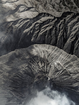 Aerial view of the rugged, grey volcanic landscape, with deep shadows and mist hugging the ridges, Mount Bromo, East Java, Indonesia.