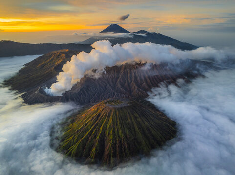 Aerial view of Mount Bromo piercing through a sea of ethereal clouds, bathed in the warm glow of the rising sun, Mount Bromo, East Java, Indonesia.