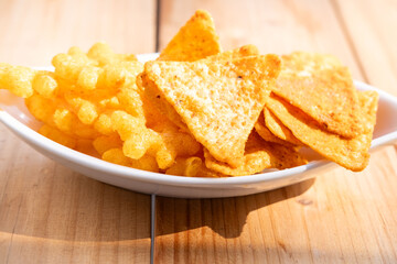 Crispy corn chips and crunchy cheese snacks in white bowl, bright sunlight, crunchy tasty fast food appetizer, unhealthy but delicious salty treat for snack time, Unhealthy but tasty fast food snack