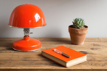 Vintage office corner with orange retro lamp, wooden desk, succulent plant in terracotta pot, orange notebook, and pen, creating cozy and nostalgic workspace vibe