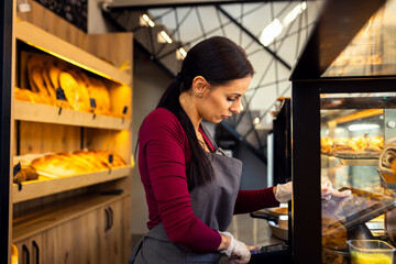 Smiling woman working in a bakery using the cash register.