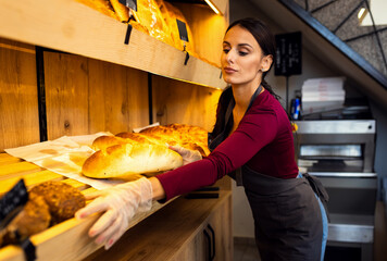 Smiling woman arranging freshly baked bread on shelves inside bakery.