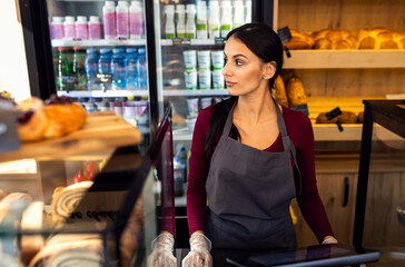 Smiling woman working in a bakery using the cash register.