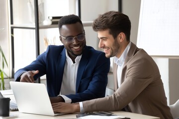 Two diverse businessmen in suits working together at laptop, smiling and discussing project in modern office. Concept of teamwork, mentoring, startup collaboration, success.