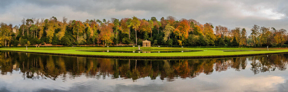Panoramic view of Studley Royal Water Garden in North Yorkshire, with autumn trees and reflective waters under soft, cloudy seasonal light