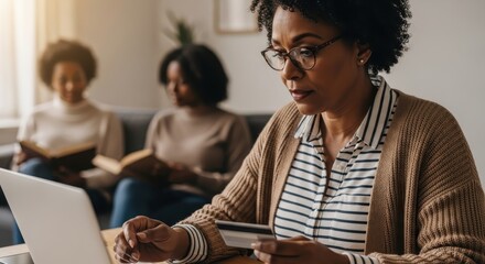 Woman shopping online using a laptop and credit card while two friends read books in the background for a relaxed atmosphere