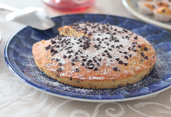 Chocolate chip cake on patterned ceramic plate. Holidays and lifestyle. Food on table covered with tablecloth. 