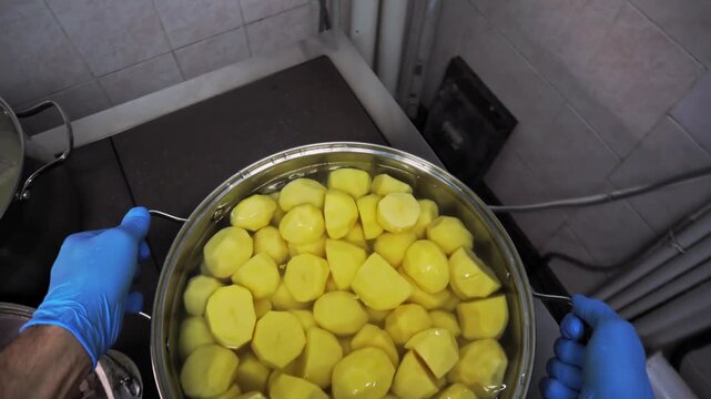A man takes a big pot of peeled potatoes and places it on a preheated stove