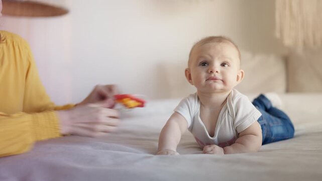 Smiling young mother playing with newborn baby girl, showing colorful teether