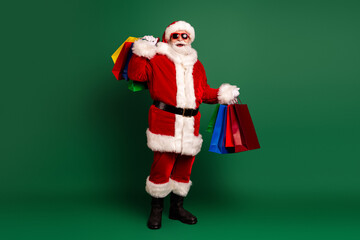 Santa Claus in classic red suit with gift bags and shopping bags on green background ready for...