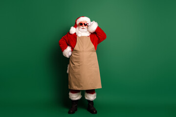 Santa in red costume with beige apron stands on a green background wearing hat and sunglasses ready for holiday shopping and festive fun