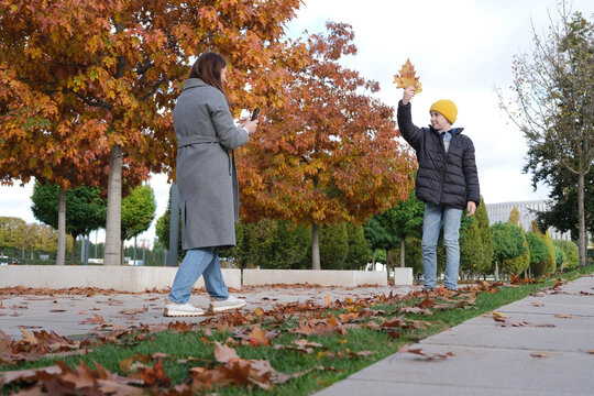 Family of mother and son collecting and photographing autumn leaves in the park
