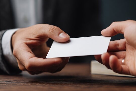 Person's hands and a client's hands exchanging a business card over a table networking and partnership initiation concept