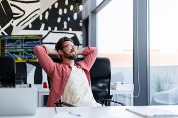 Fototapeta premium Smiling middle aged man wearing stylish eyeglasses, sitting on workplace relaxing looking away