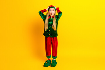 Excited young girl in festive elf costume standing on vibrant yellow background portraying joyful Christmas cheer