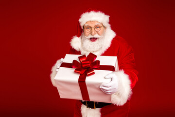 Naklejka premium Santa Claus delivers a festive Christmas gift box full of joy to a bright red background capturing holiday magic warmth and family celebration