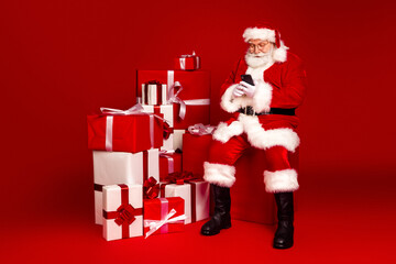 Santa Claus sits among wrapped gifts using a smartphone creating a festive holiday moment perfect for Christmas shopping and family celebration