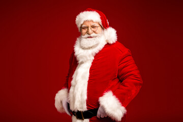 Santa Claus in red suit with white fur trim smiles confidently against a rich red background ready for holiday celebration and seasonal shopping