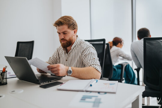 A focused office worker sits at a clean desk, examining papers beside a laptop. The scene conveys professionalism, productivity, and a modern, collaborative workspace.