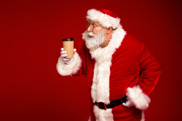 Santa in a red suit with coffee cup exudes festive cheer against bold red backdrop perfect for Christmas ads and holiday campaigns