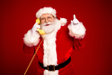 Santa on a red backdrop chats on a bright yellow phone sharing a merry moment with a raised finger