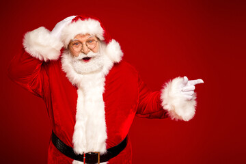 Santa Claus in a bright red costume smiles and points against a solid red background perfect for Christmas holidays family celebration