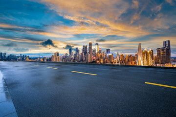 Obraz premium Empty wet asphalt road with a view of the modern city skyline and financial district at sunset.