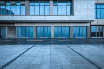 Empty stone pavement in front of a modern commercial building with large blue glass doors and windows after the rain.