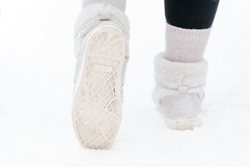 young caucasian woman walking on white snow in winter, white and pink shoes close-up view,, back view