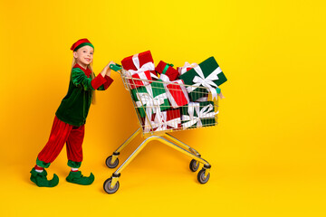 Girl dressed as elf with gifts in shopping cart promoting a festive holiday spirit against a bright yellow background