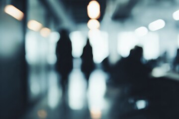 A blurred image showing silhouettes of people in a modern, softly lit indoor environment, creating an abstract and atmospheric feel.