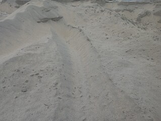 Vast expanse of granular sand dunes under natural daylight, showcasing textured earth and geological formations ideal for construction or environmental concepts.