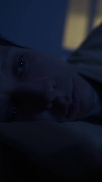 Man lying awake at night, warm yellow window light, insomnia night scene, close-up vertical video