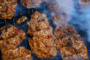 Close-up of juicy meat patties sizzling on a smoky grill. Showcasing barbecue cooking and delicious outdoor food preparation with flavorful spices. The barbecue smoke adds a creative touch.