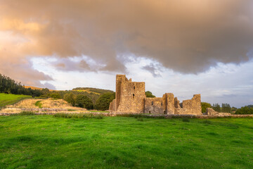 Fototapeta premium Historic Fore Abbey ruins under soft light. Solitary stone walls on rolling green hills. Quaint heritage site bathed in warm sunset hues amidst lush countryside and dramatic skies, Ireland